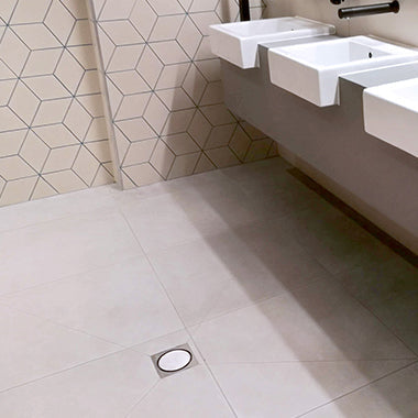 A stainless steel shower drain grate designed for tiled floors.