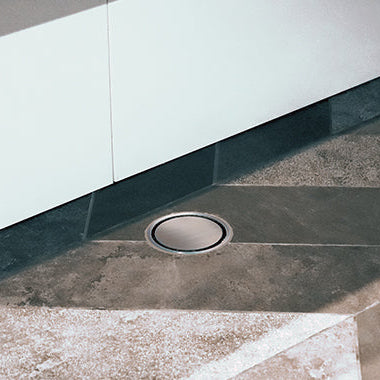 A stainless steel shower drain grate show on a tiled floors.