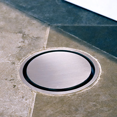 A stainless steel shower drain grate on tiled floor