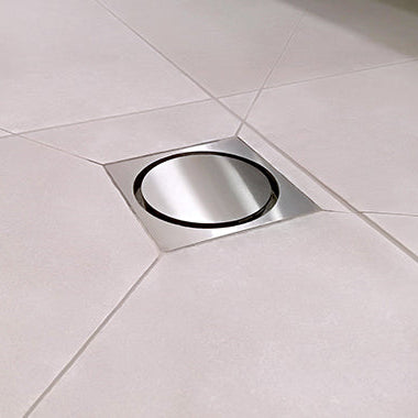 A stainless steel shower drain grate on white tiles.